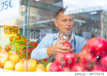 Salesman working behind glass showcase of greengrocery Salesman working behind glass showcase of greengrocery 96778216