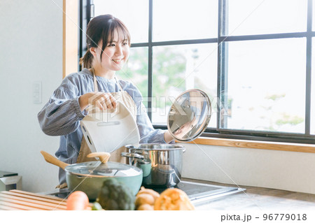 キッチンで電気ケトルのお湯を鍋に入れるエプロン姿のアジア人女性 96779018