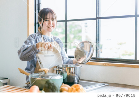 キッチンで電気ケトルのお湯を鍋に入れるエプロン姿のアジア人女性 キッチンで電気ケトルのお湯を鍋に入れるエプロン姿のアジア人女性 96779019