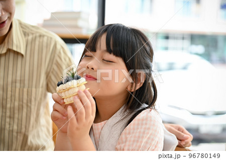 Happy cute Asian little girl enjoys eating cake or dessert at the cafe coffee shop with her dad. 96780149