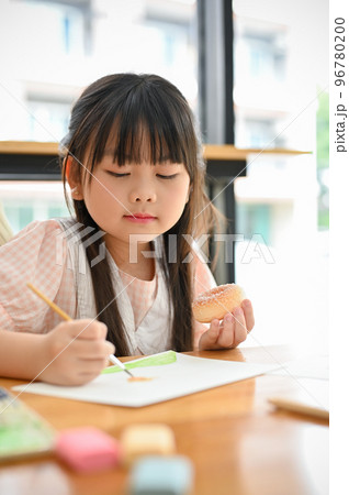 An adorable young Asian girl drawing and painting with a watercolor on a paper at home 96780200