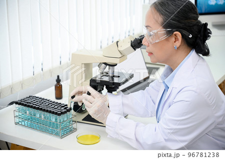 A professional asian-aged female scientist examining a virus specimen under a microscope A professional asian-aged female scientist examining a virus specimen under a microscope 96781238