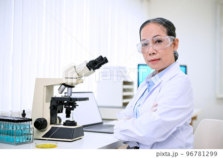 Confident senior Asian female scientist or chemist in white gown at her desk in the laboratory. 96781299