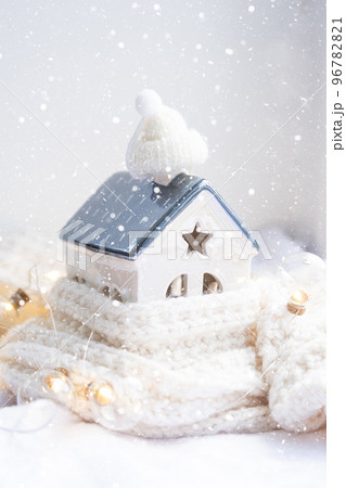 Cozy house is wrapped in a hat and scarf in a snowstorm -window sill decor. Winter, snow - home insulation, protection from cold and bad weather, room heating system. Festive mood, Christmas, New Year Cozy house is wrapped in a hat and scarf in a snowstorm -window sill decor. Winter, snow - home insulation, protection from cold and bad weather, room heating system. Festive mood, Christmas, New Year 96782821
