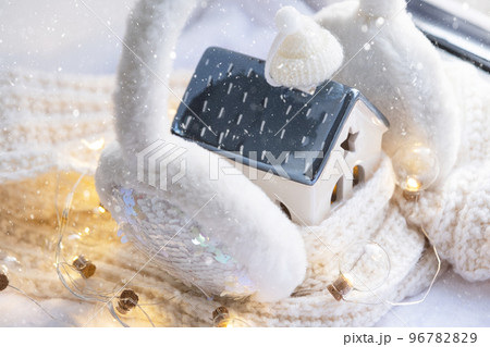 Cozy house is wrapped in a hat and scarf in a snowstorm -window sill decor. Winter, snow - home insulation, protection from cold and bad weather, room heating system. Festive mood, Christmas, New Year 96782829
