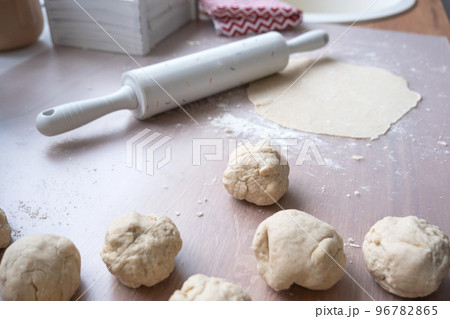 Hands knead thick dough, roll out with a rolling pin on the kitchen table, decorated with festive decorations for Christmas and New year. Baking at home, aroma and comfort. Hands knead thick dough, roll out with a rolling pin on the kitchen table, decorated with festive decorations for Christmas and New year. Baking at home, aroma and comfort. 96782865