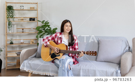 Asian female artist playing the guitar and singing happily in the living room, Relaxation with music therapy, Spending free time with music, Joy of playing music, Acoustic guitar. Asian female artist playing the guitar and singing happily in the living room, Relaxation with music therapy, Spending free time with music, Joy of playing music, Acoustic guitar. 96783263