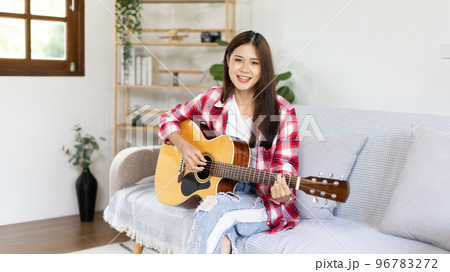 Asian female artist playing the guitar and singing happily in the living room, Relaxation with music therapy, Spending free time with music, Joy of playing music, Acoustic guitar. Asian female artist playing the guitar and singing happily in the living room, Relaxation with music therapy, Spending free time with music, Joy of playing music, Acoustic guitar. 96783272