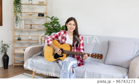 Asian female artist playing the guitar and singing happily in the living room, Relaxation with music therapy, Spending free time with music, Joy of playing music, Acoustic guitar. Asian female artist playing the guitar and singing happily in the living room, Relaxation with music therapy, Spending free time with music, Joy of playing music, Acoustic guitar. 96783273