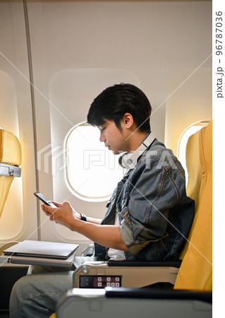 Hipster Asian male traveler or passenger in an economy seat, using his smartphone 96787036