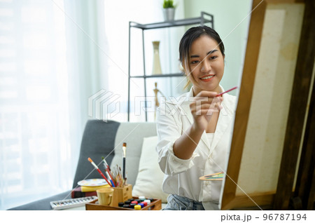 Charming Asian female painter painting her creative artwork on canvas easel in her studio 96787194