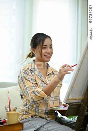 Portrait, Cheerful Asian woman artist sitting in front of easel in her workshop. creativity hobby Portrait, Cheerful Asian woman artist sitting in front of easel in her workshop. creativity hobby 96787207