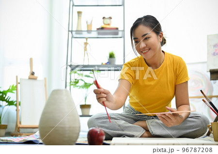 Talented and creative young Asian woman measuring her design with paintbrush Talented and creative young Asian woman measuring her design with paintbrush 96787208