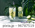 Cool lavender lemonade with lime slices and lavender flower on the table near dark green wall and palm leaves. Healthy organic summer soda drink. Detox water. Diet unalcolic coctail. 96787519