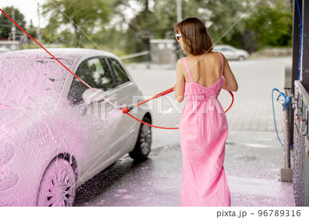 Woman in pink dress washing her tiny car with nano foam at car wash 96789316