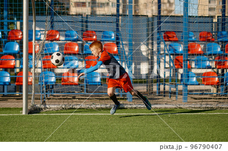 Junior goalkeeper catching ball while defending gate in football match Junior goalkeeper catching ball while defending gate in football match 96790407