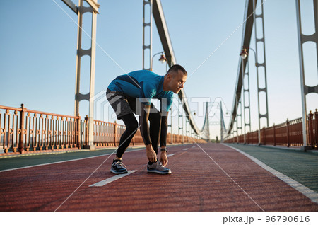 Young athlete man tying lace on running shoes during training on city bridge 96790616