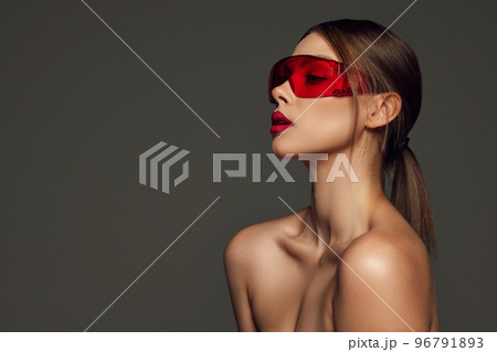 Sensual young woman with naked shoulders and well-kept skin wearing trendy red eyewear posing over dark grey background. Beauty, fashion, style 96791893