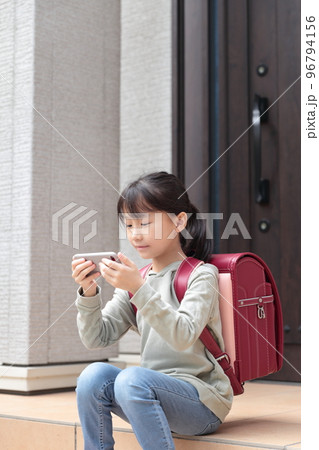 放課後に玄関で座ってスマホを見る小学生 96794156
