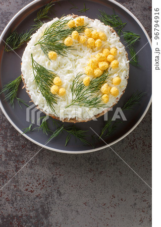 Round formed mimosa salad with vegetables, eggs and canned fish closeup on gray plate. Vertical top view 96794916