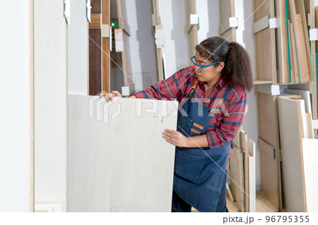 A middle aged woman pulling plywood from a storage compartment. Asian carpenter worker work in a furniture factory. A middle aged woman pulling plywood from a storage compartment. Asian carpenter worker work in a furniture factory. 96795355