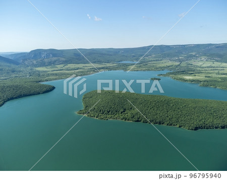 Aerial view on mountain lake. Drone over water reservoir at mountain valley covered with green spring forest. Beautiful view from above on smooth blue surface of mountain lake among highlands. Nobody Aerial view on mountain lake. Drone over water reservoir at mountain valley covered with green spring forest. Beautiful view from above on smooth blue surface of mountain lake among highlands. Nobody 96795940