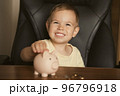Child puts coins in piggy bank. Smart happy boy saving money in a piggy bank, learning about saving 96796918
