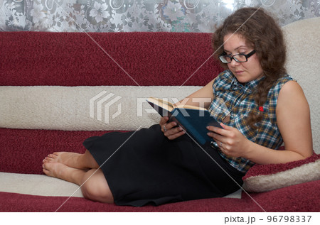 Woman with curly hair reading a book on sofa Woman with curly hair reading a book on sofa 96798337