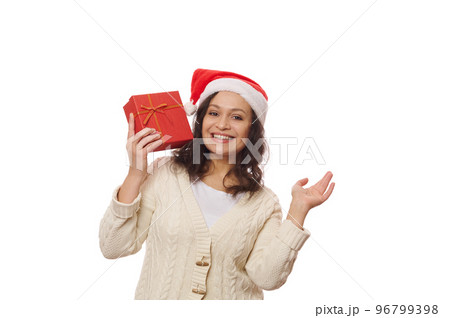 Latin American beautiful woman in Santa hat with Xmas gift box, smiling a toothy smile looking at camera, isolated on white background. Time to unpack Christmas and New Year's presents. Boxing Day 96799398