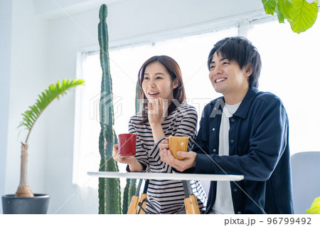 明るいリビングでコーヒーを飲む若い笑顔の会話する夫婦 96799492
