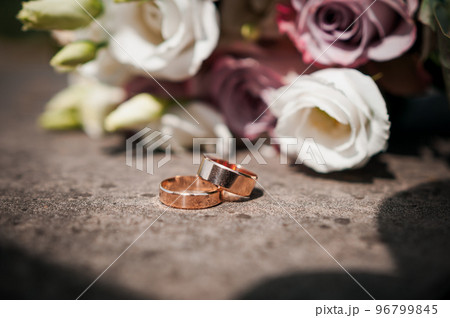 A pair of gold wedding rings, a bouquet of flowers in the background A pair of gold wedding rings, a bouquet of flowers in the background 96799845