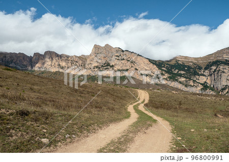 Old path through mountains. Trekking mountain trail. Bright atmospheric minimalist alpine landscape with stony footpath among grasses in highlands. Pathway uphill. Way up mountainside. 96800991