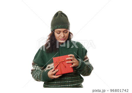Beautiful dark-haired Latin American woman in green warm wool Xmas patterned sweater and hat, with Christmas red gift box, isolated on white background. Time to open festive presents. Happy New Year 96801742