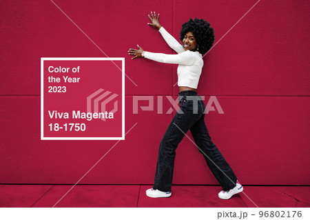 Smiling fashionable american woman walking on city street. Color of the year 2023, viva magenta. 96802176