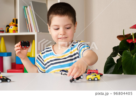 A preschool child plays with toy cars sitting at a table at home. A preschool child plays with toy cars sitting at a table at home. 96804405