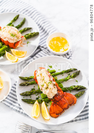Sering garlic lobster tails with steamed asparagus and lemon wedges on a white plate. Sering garlic lobster tails with steamed asparagus and lemon wedges on a white plate. 96804778