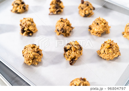 Scooping cookie dough with dough scoop into a baking sheet lined with parchment paper to bake soft oatmeal raisin walnut cookies. Scooping cookie dough with dough scoop into a baking sheet lined with parchment paper to bake soft oatmeal raisin walnut cookies. 96804797
