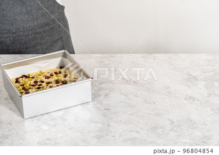 Filling square cheesecake pan lined with parchment paper with fudge mixture to prepare cranberry pistachio fudge. 96804854
