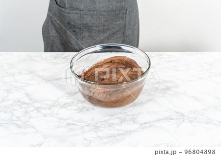 Mixing store-bought chocolate frosting in a mixing glass bowl with a hand mixer. Mixing store-bought chocolate frosting in a mixing glass bowl with a hand mixer. 96804898