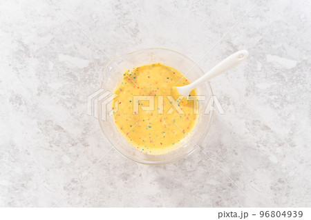 Flat lay. Mixing ingredients in a glass mixing bowl to bake funfettti bundt cake. 96804939