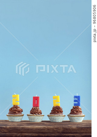 Happy New Year 2023 theme. Homemade chocolate cupcakes with 2023 number colorful candle on wooden table. Vertical frame, blue background. 96805906