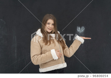 Happy young woman in beige sheepskin coat poses on black background. Heart above hand. Space for text. Winter clothing 96806054