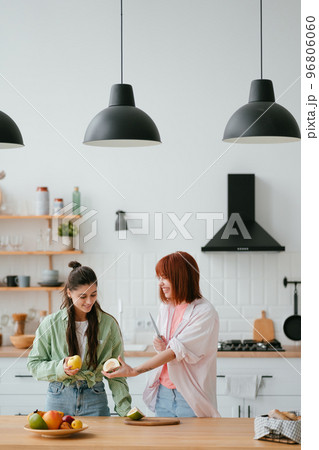 Two girlfriends cut fruit in the kitchen Two girlfriends cut fruit in the kitchen 96806060