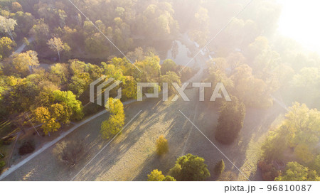 Aerial flying over trees with yellow leaves, meadow, dirt road with morning mist an autumn sunny morning in park. Bright sunlight, shining sunbeams rays, sun overexposure. Beautiful natural background 96810087