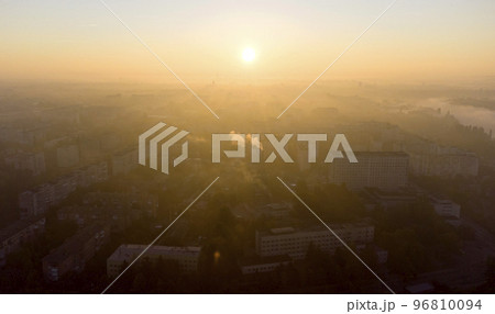 Forest park trees, river and many high-rise buildings in city in early morning at dawn in summer. Brightly shining sun, clear cloudless sky and morning mist Sunbeams and shadows Aerial drone landscape Forest park trees, river and many high-rise buildings in city in early morning at dawn in summer. Brightly shining sun, clear cloudless sky and morning mist Sunbeams and shadows Aerial drone landscape 96810094