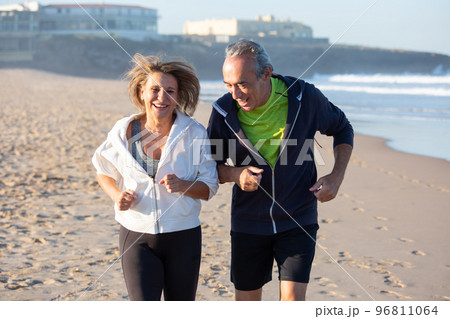 Cheerful senior couple laughing while running on seashore 96811064