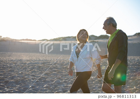 Cheerful man and woman smiling while walking along seashore 96811313