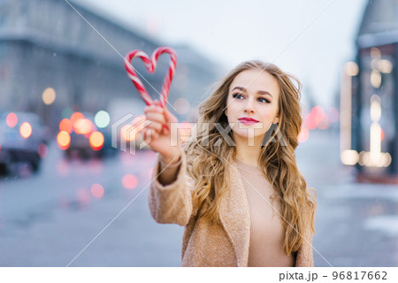 A sweet dreamy girl, a young woman holding a lollipop in the form of a heart on a winter day. The concept of Christmas or Valentine's Day A sweet dreamy girl, a young woman holding a lollipop in the form of a heart on a winter day. The concept of Christmas or Valentine's Day 96817662