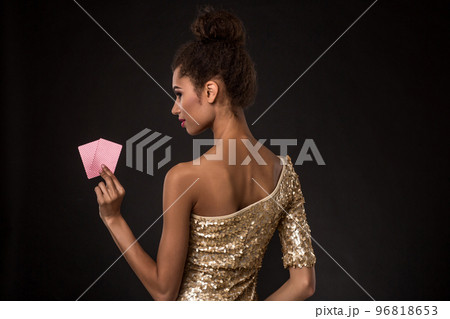 Woman winning - Young woman in a classy gold dress holding two cards, a poker of aces card combination. 96818653