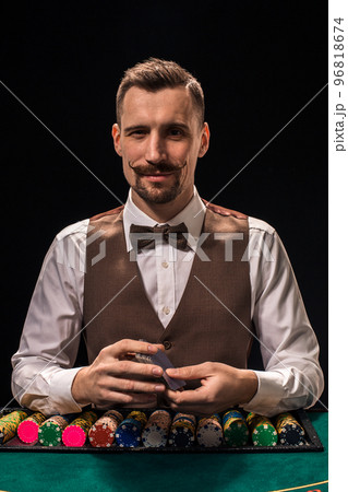 Portrait of a croupier is holding playing cards, gambling chips on table. Black background 96818674